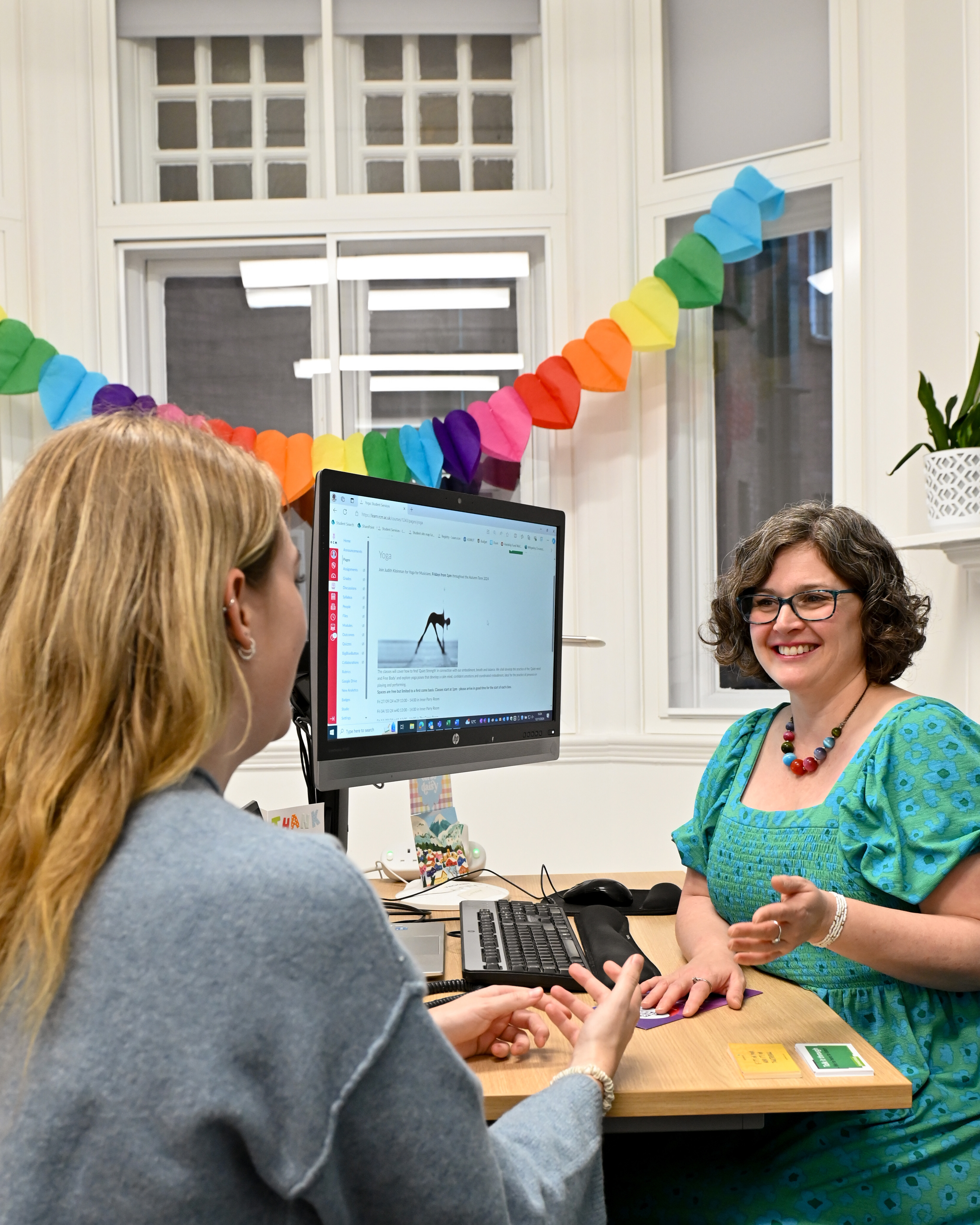 A women with brown hair, talking to a student with blonde hair in an office.